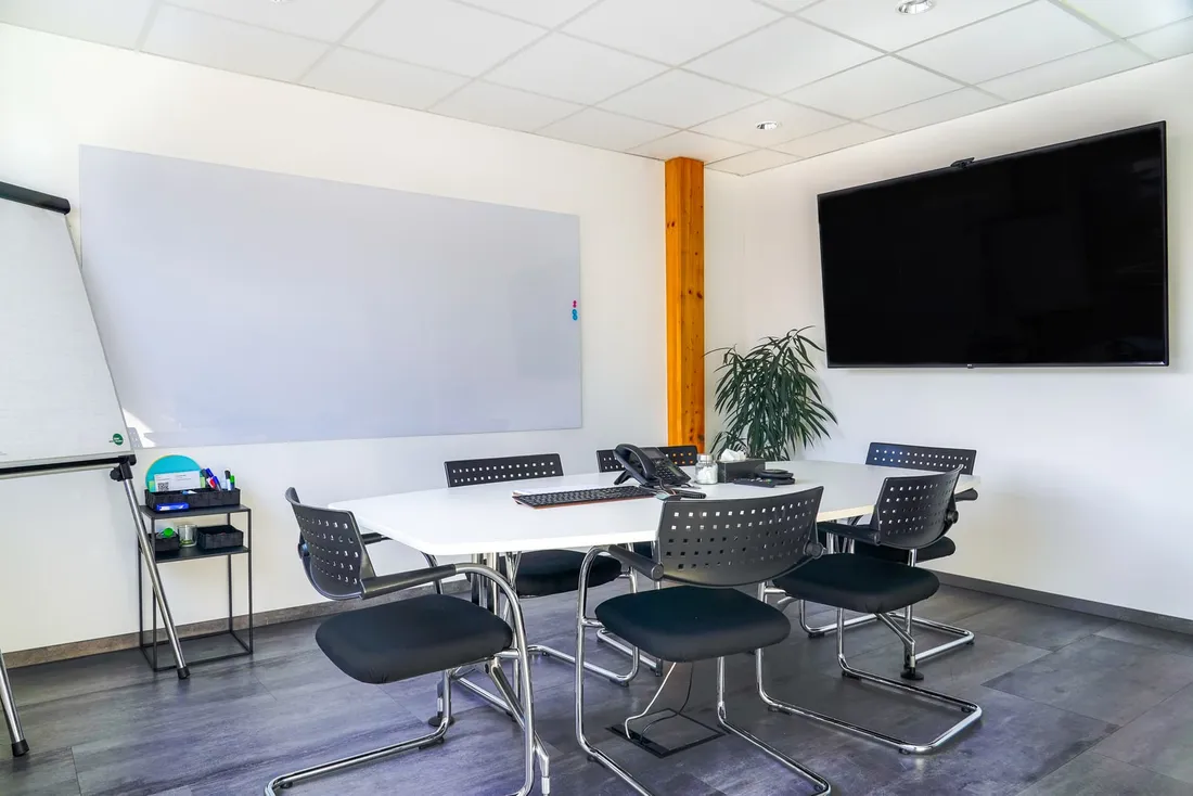 Besprechungsraum mit großem Tisch, Whiteboard, Flipchart und Wandbildschirm